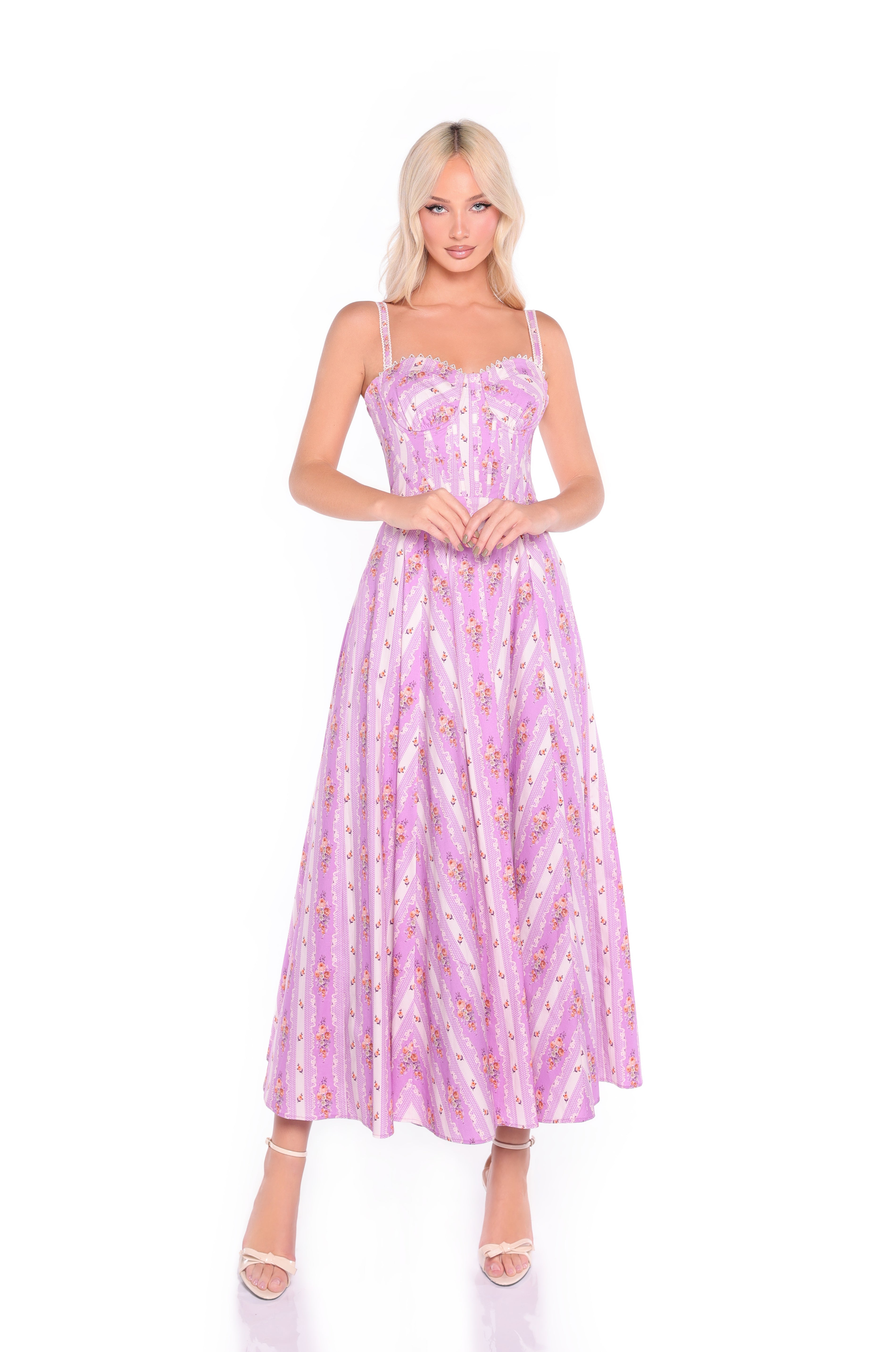 A woman stands against a white background wearing the Rosella Lavender Lilac Floral Casual Midi Dress, a sleeveless midi dress with thin straps, floral patterns, and a corset bodice, paired with open-toe heels.